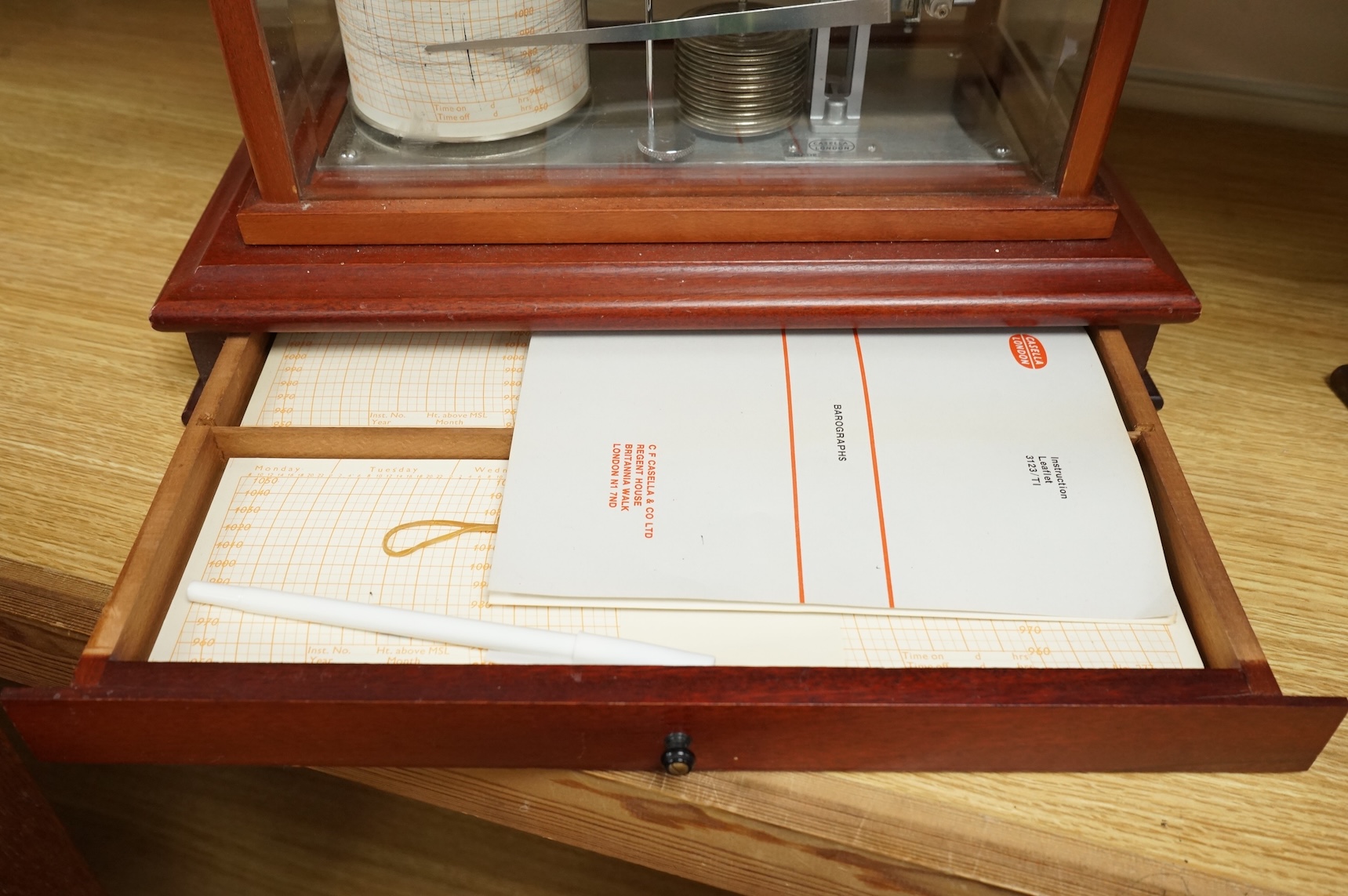 A 1970s Casella mahogany cased barograph with bevelled glass panels and a drawer underneath containing a good quantity of paper slips and instruction leaflet.